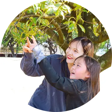 先生と生徒が一緒に木の枝を指さしながら、自然の中で学んでいる様子