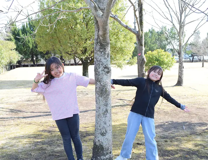 原っぱの木の横で仲良く写真に映る子どもたち